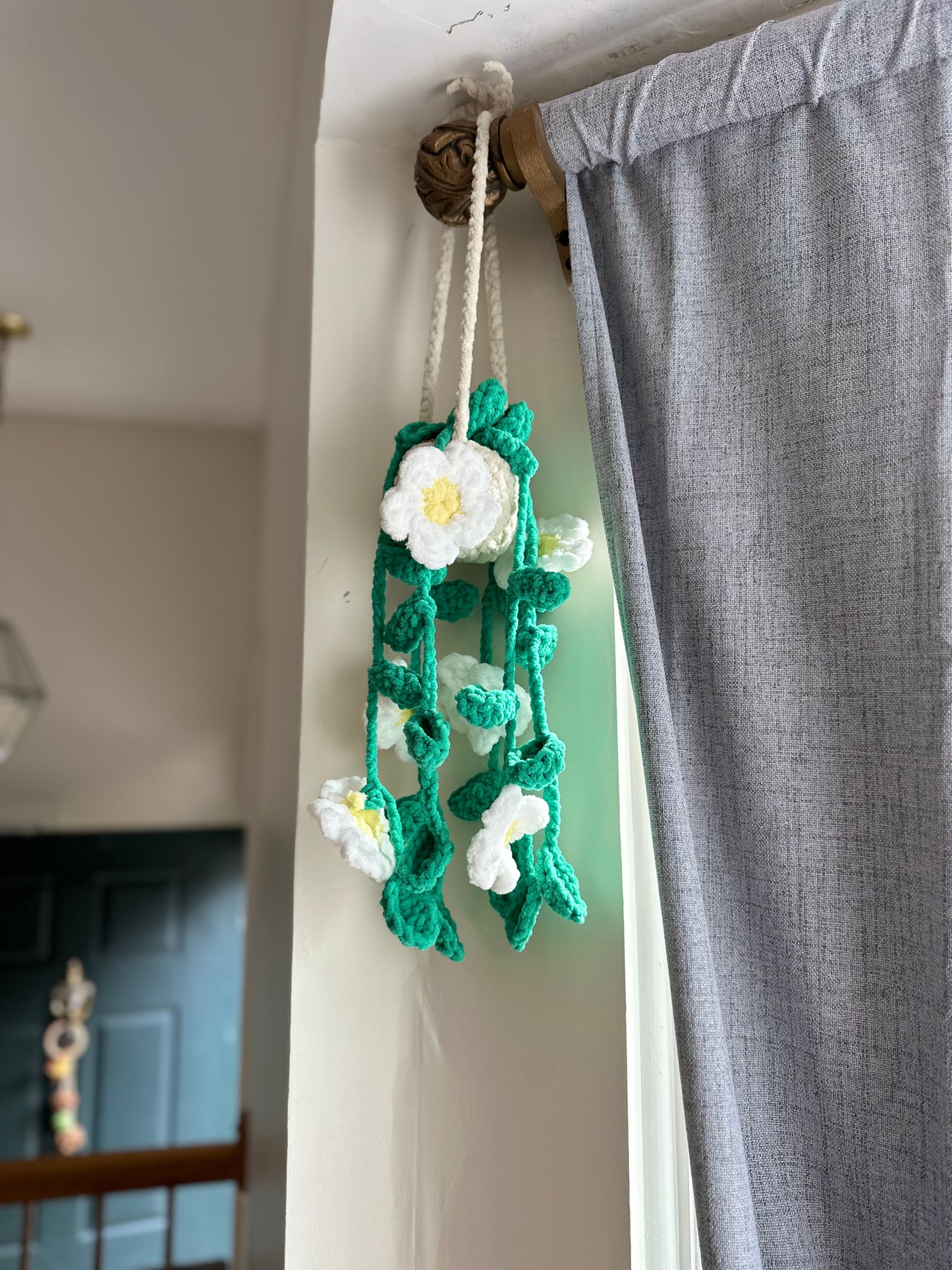 Handmade crochet flower wall hanging on a string against a neutral background.