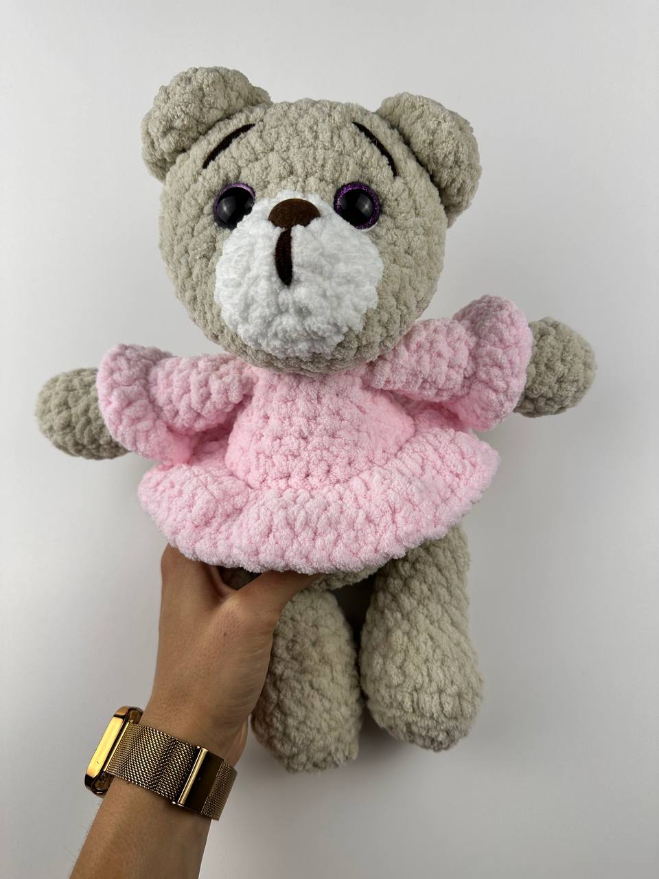 Beige crochet teddy bear wearing a pink dress, handmade from plush yarn.