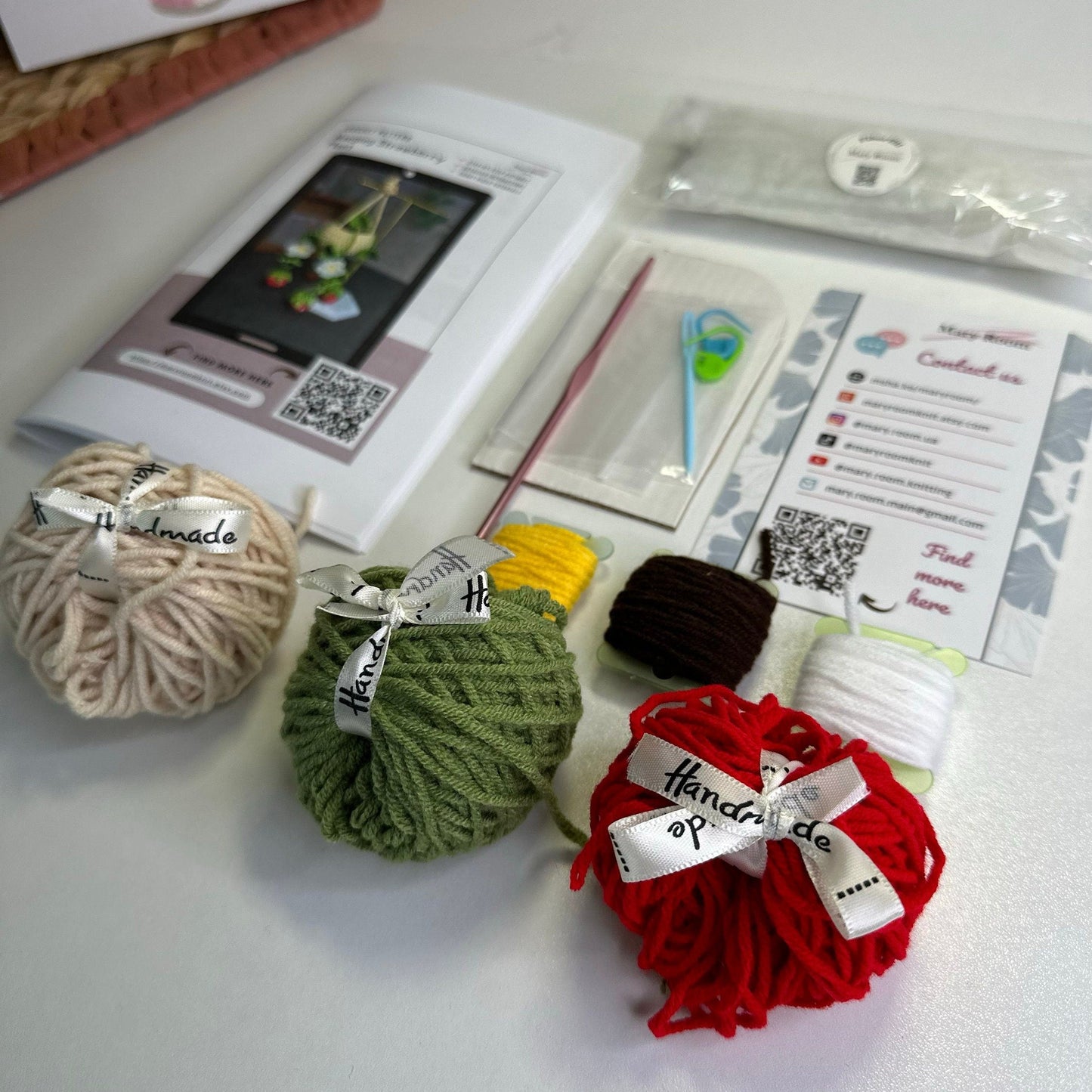 Flat lay showing red, green, cream yarn balls, cardboard, fiberfill, and crochet hook for strawberry kit