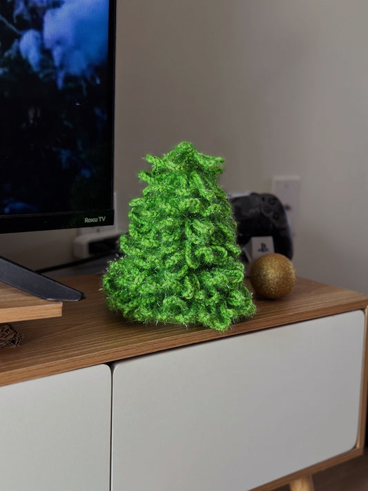 Handmade crochet Christmas tree made with shiny green yarn, standing on a wooden shelf
