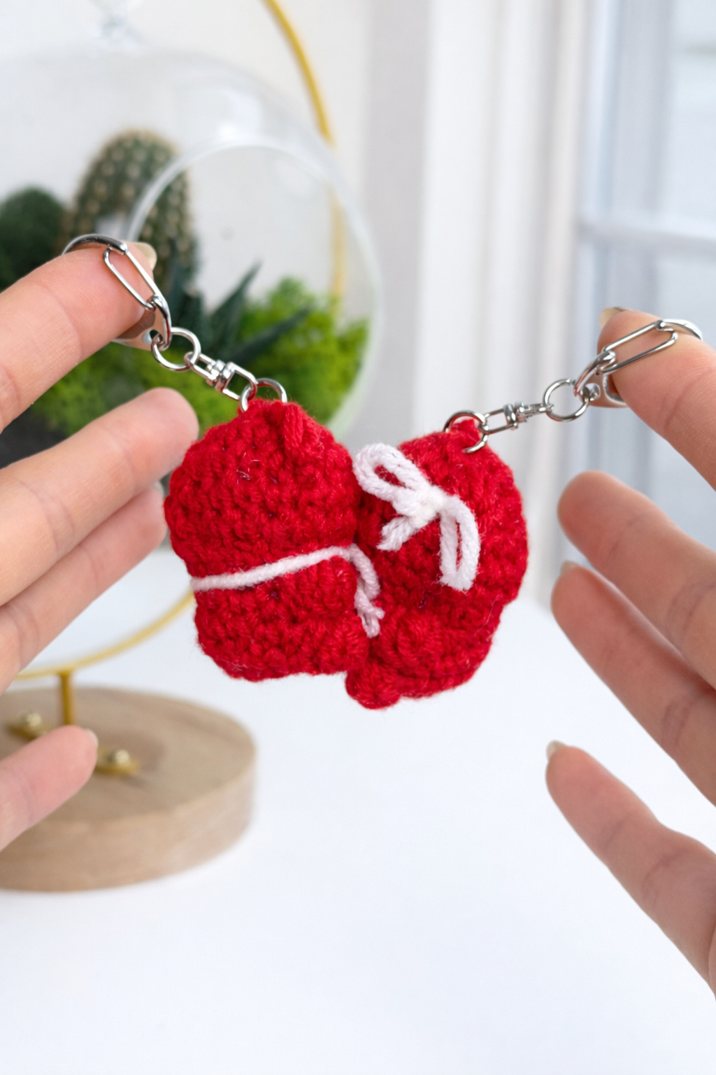 Two small red crochet bears “kissing” with keyrings, held near a plant – DIY Crochet Kit for Valentine’s Day (Kissing Bears)