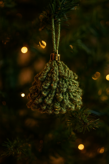 Green crochet Christmas ornament with metallic yarn hanging on a Christmas tree with warm lights