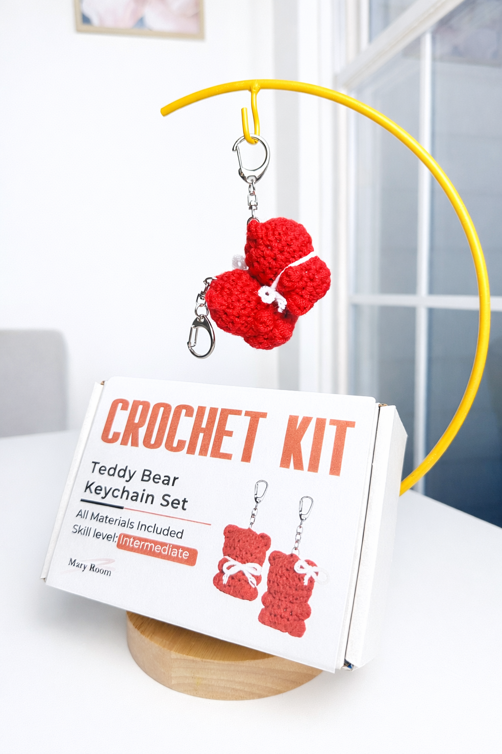 Crochet keychain bear displayed on a white stand next to kit packaging box – DIY Crochet Kit for Valentine’s Day (Kissing Bears)