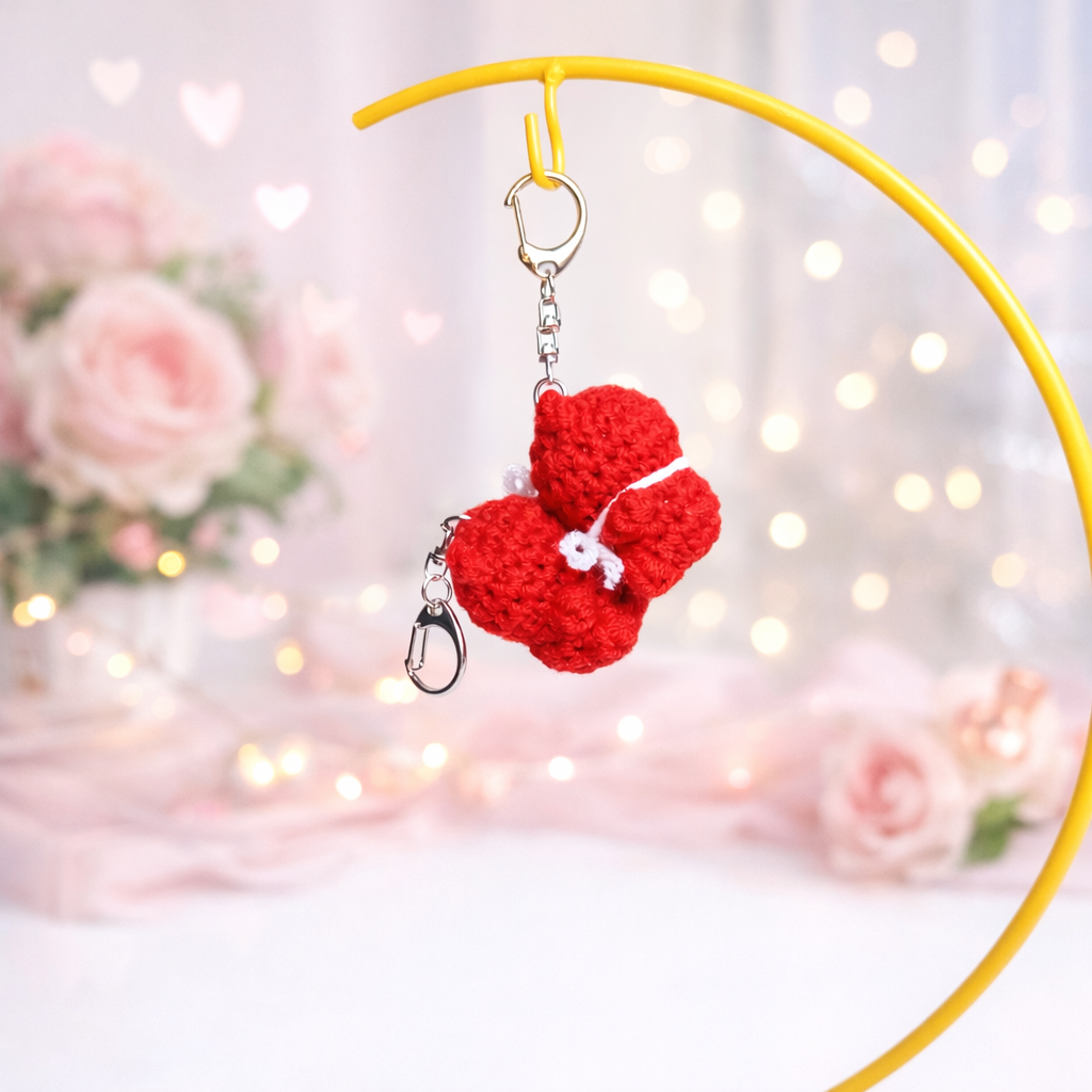 Crochet bear keychain hanging from a yellow ring in front of soft pink background with flowers – DIY Crochet Kit for Valentine’s Day (Kissing Bears)