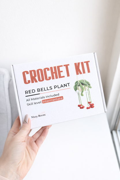 Holding the product box labeled DIY Crochet Kit Red Bells Plant, white minimal background.