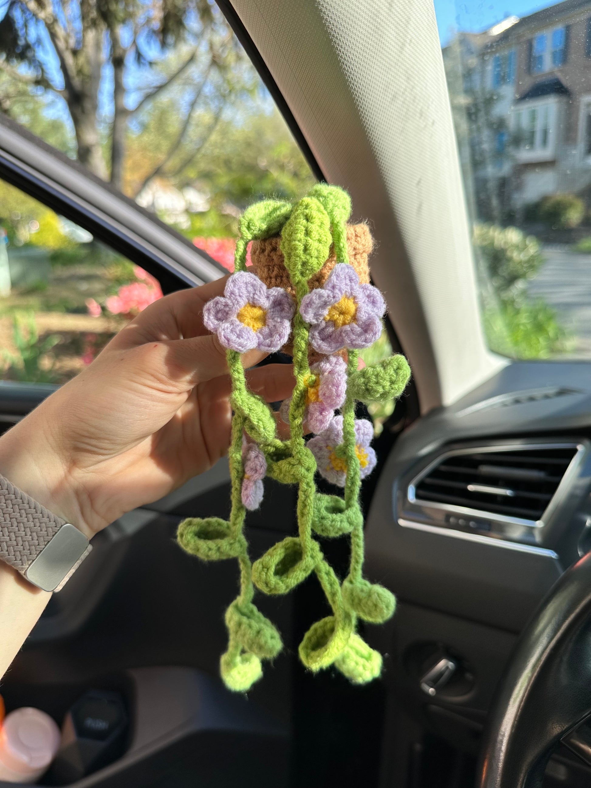 Hand holding a crocheted flower decoration inside a car