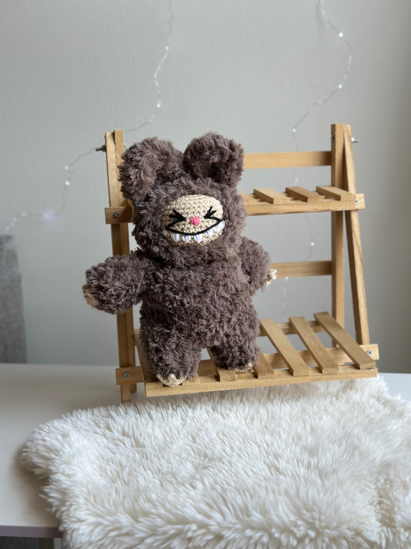 Brown faux fur Labubu plushie sitting alone on a mini wooden bench, highlighting its fuzzy texture.
