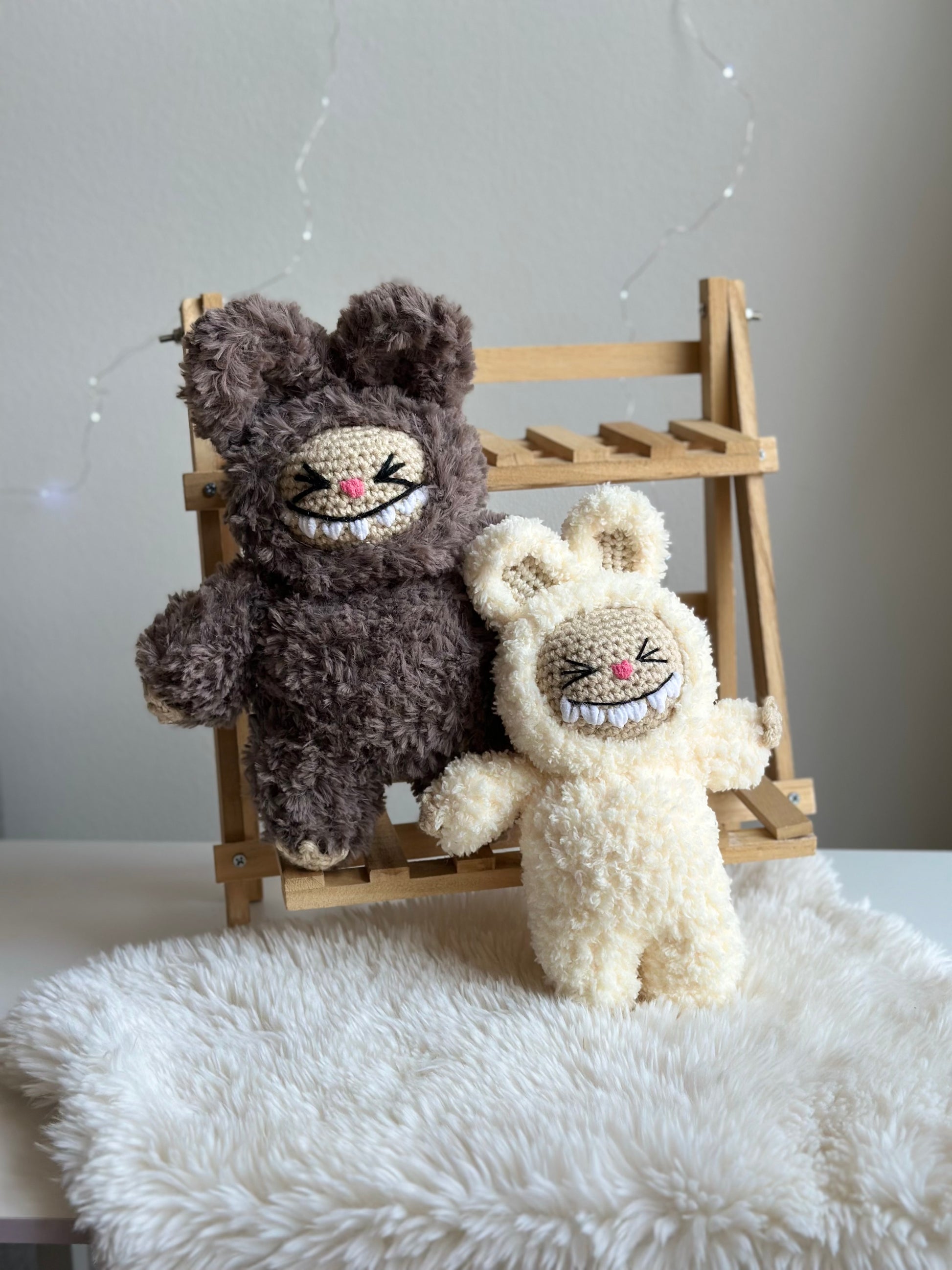 Two crocheted Labubus in sherpa (cream) and fluffy yarn (brown) seated together for comparison. Crochet pattern