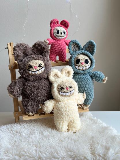Group shot of three Labubus made from sherpa, classic yarn, and plushie yarn sitting on faux fur background. Crochet pattern
