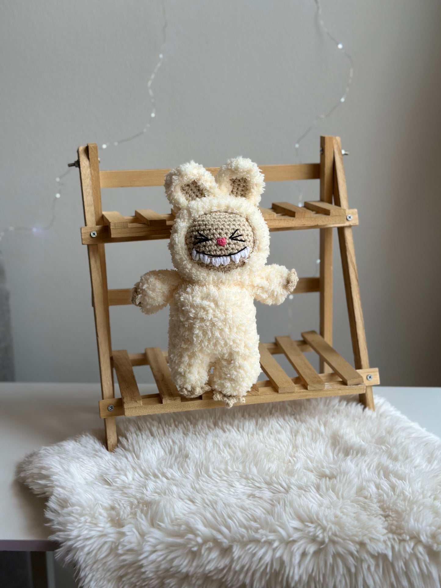 Close-up of one crocheted Labubu made with soft sherpa yarn, seated on wood bench with white fur background. crochet pattern