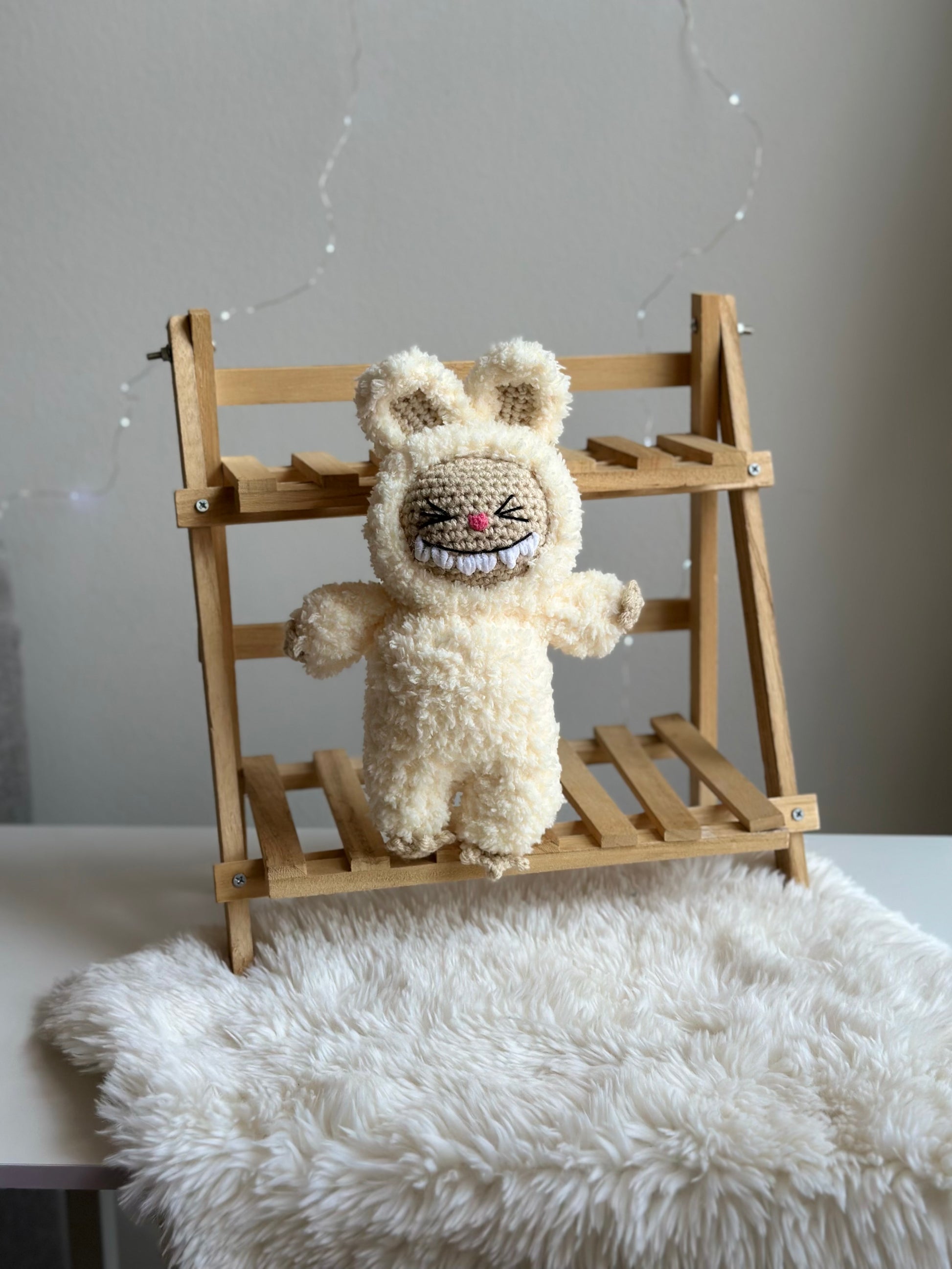 Close-up of one crocheted Labubu made with soft sherpa yarn, seated on wood bench with white fur background. crochet pattern