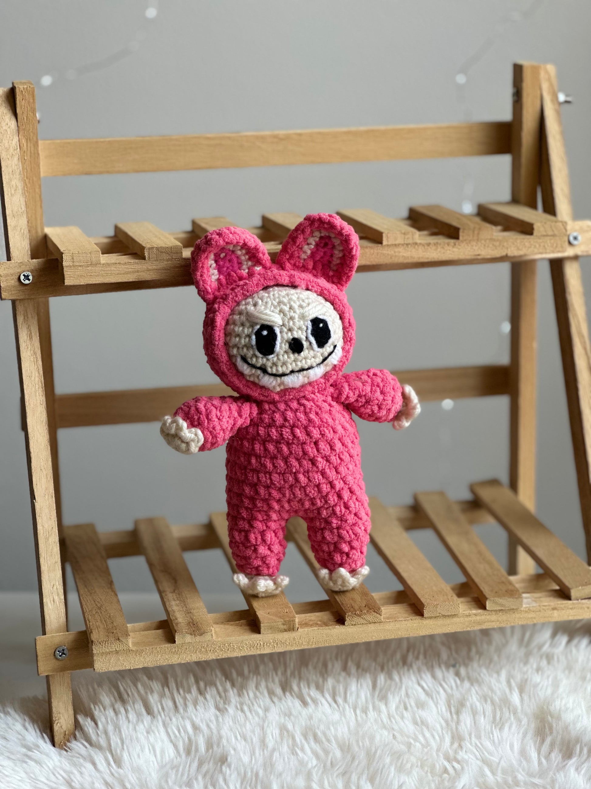 Pink Labubu plushie made with standard acrylic yarn displayed on a small wooden bench.