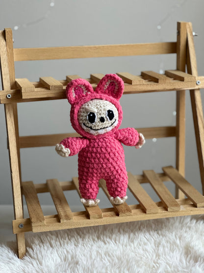 Pink Labubu plushie made with standard acrylic yarn displayed on a small wooden bench.