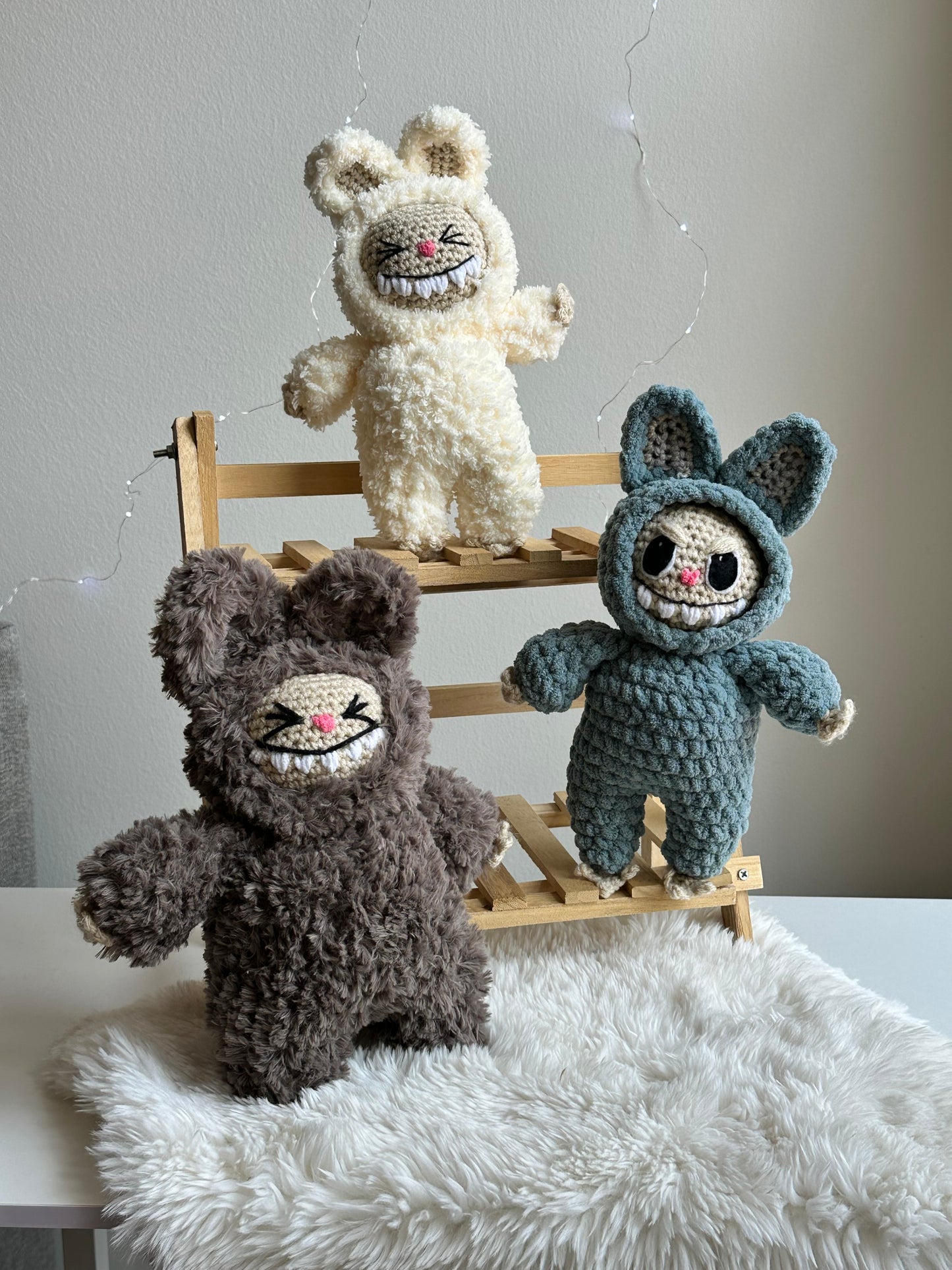 Group shot of three Labubus made from sherpa, classic yarn, and plushie yarn sitting on faux fur background.