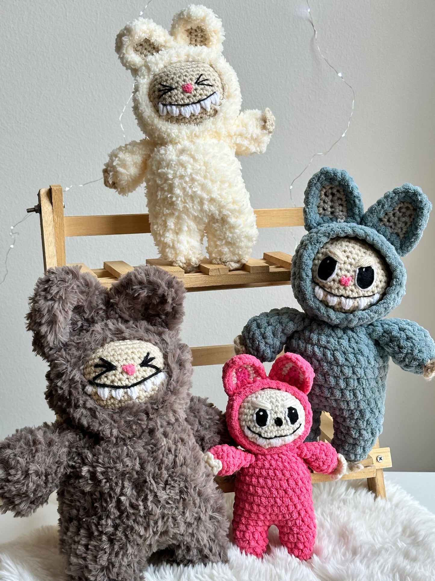 Full set of four crocheted Labubu dolls made with different yarn textures: plushie, sherpa, faux fur, and classic. Displayed together on wooden shelf.