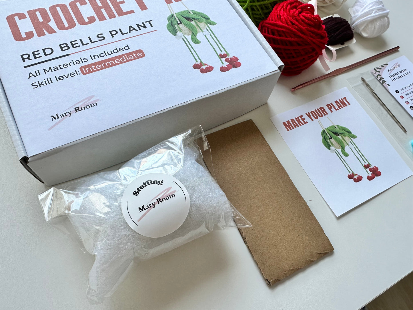 Flat lay of all packed items from DIY Crochet Kit Red Bells Plant including yarn, stuffing, and instruction booklet.