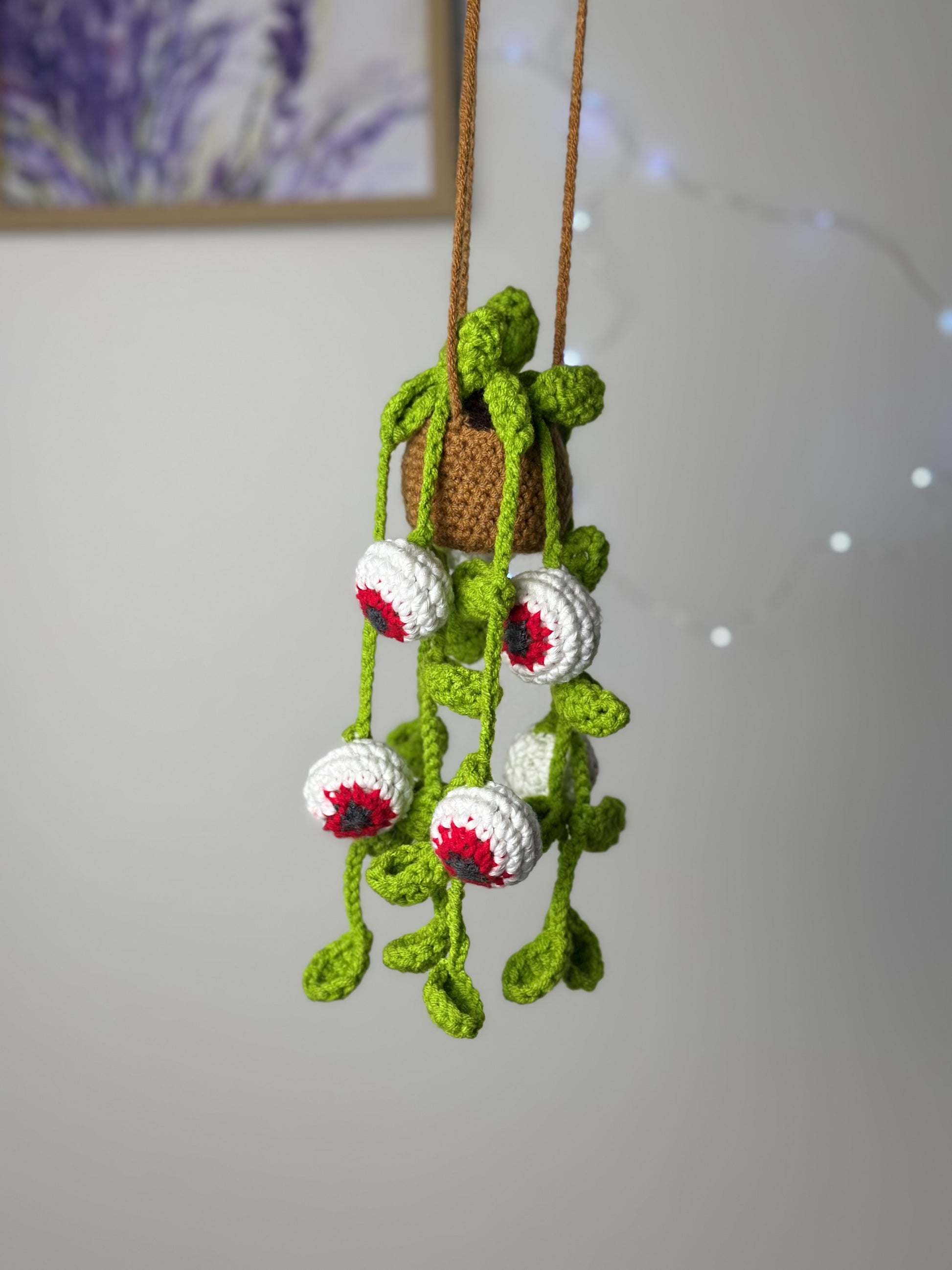 Crocheted spooky eyes plant with hanging vines and glowing eyeballs displayed with fairy lights on neutral background
