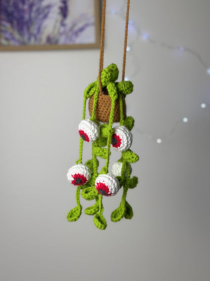 Crocheted spooky eyes plant with hanging vines and glowing eyeballs displayed with fairy lights on neutral background
