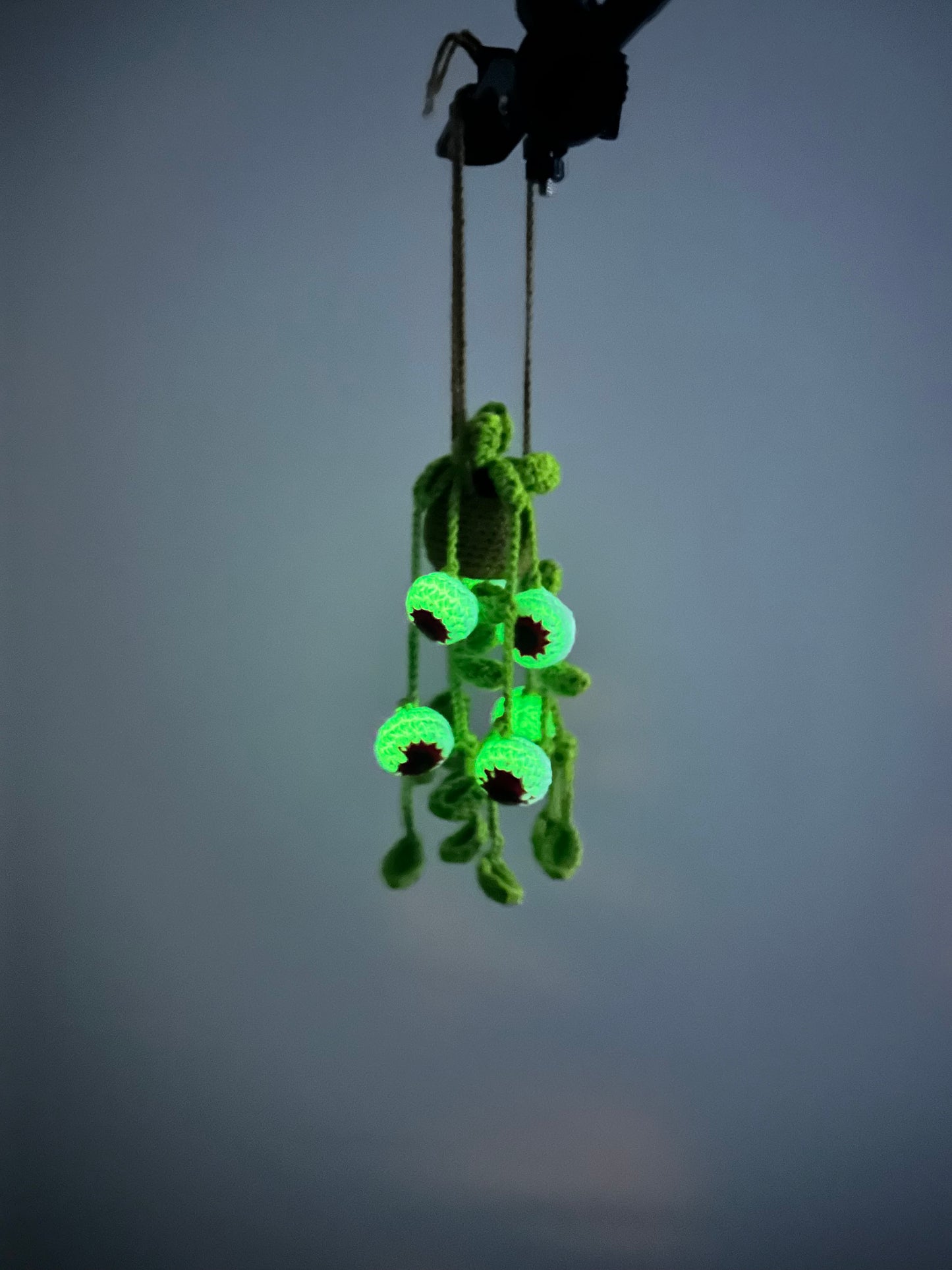 Crocheted spooky eyes plant with hanging vines and glowing eyeballs displayed with fairy lights on neutral background
