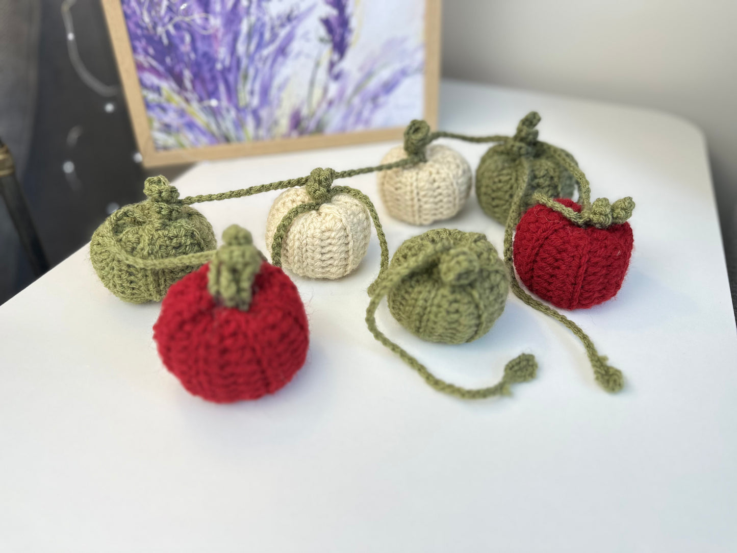 Crocheted pumpkins in red, green, and white on a white surface with a blurred background.