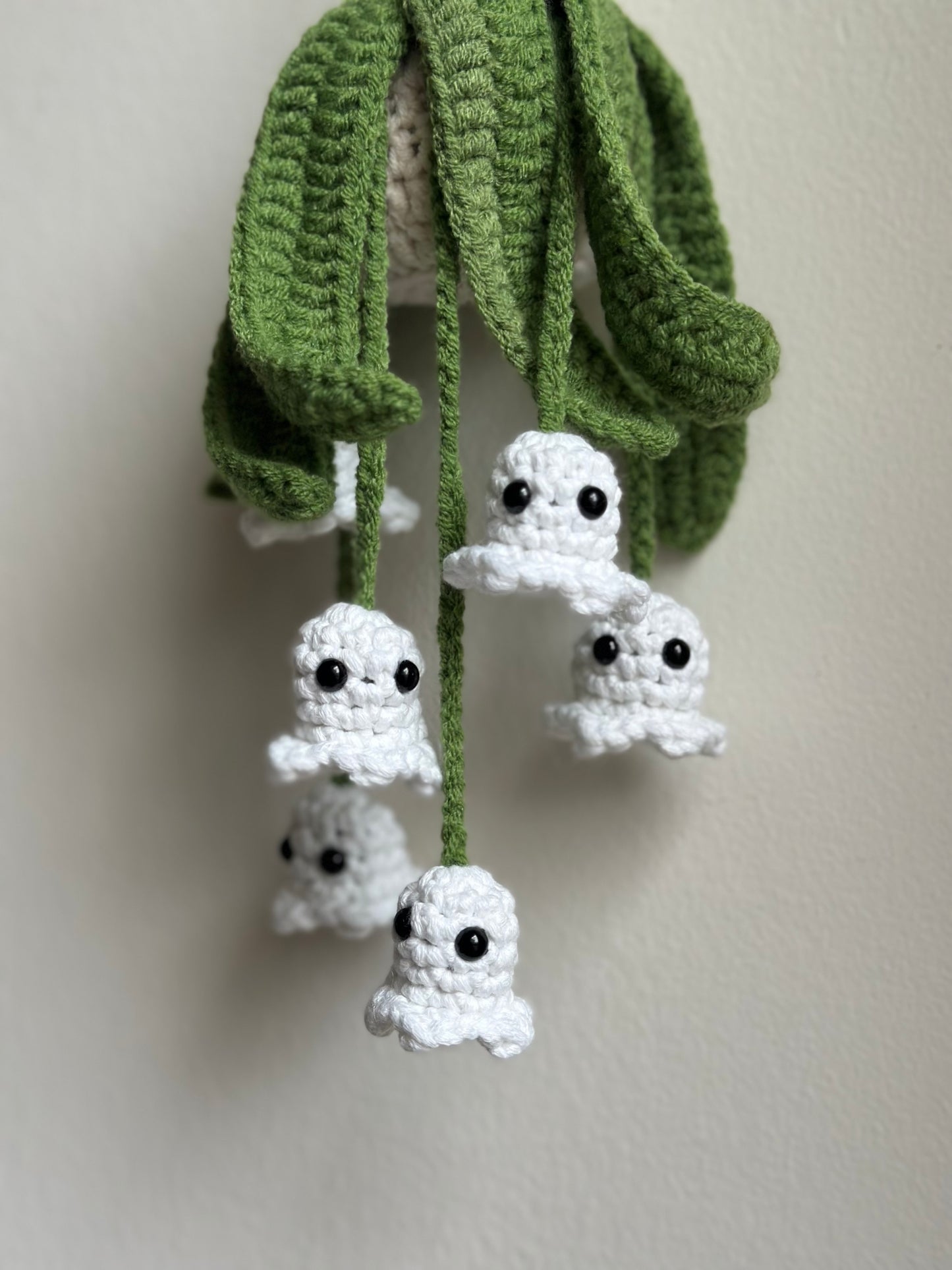 Close-up of handmade crochet ghosts with hanging green leaves.