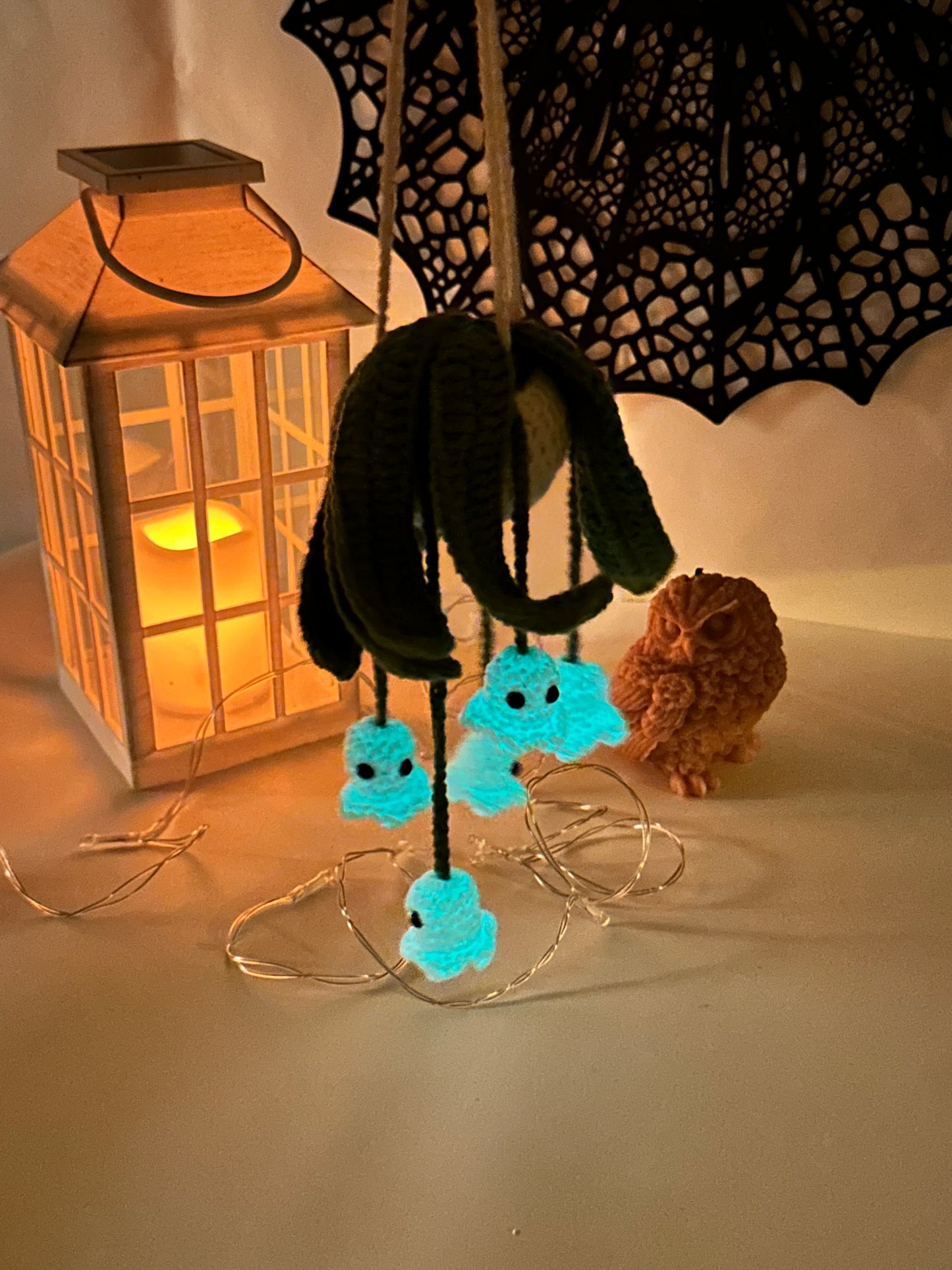 Crochet ghost hanging plant displayed with Halloween decor and candle lantern — crochet Halloween pattern idea.