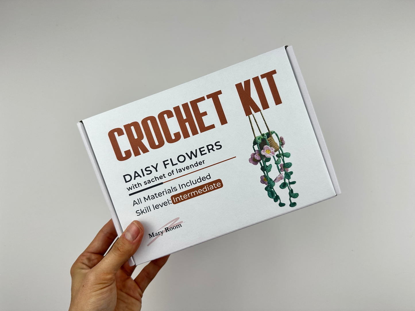 Crochet kit hanging daisy flowers plant packaging with floral design and text on a gray background