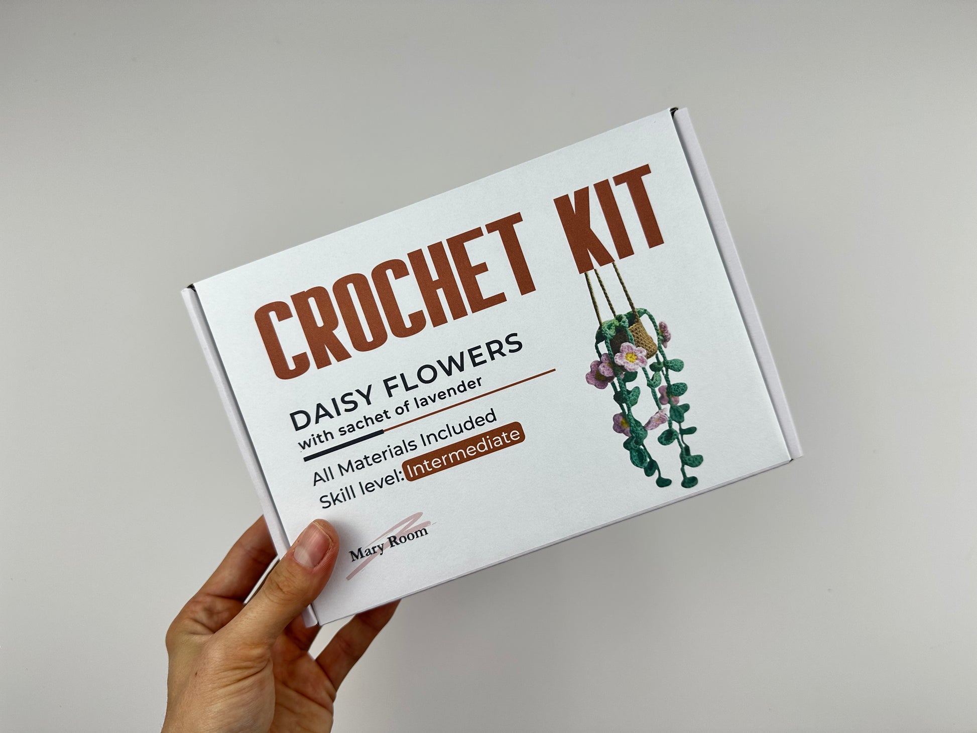 Crochet kit hanging daisy flowers plant packaging with floral design and text on a gray background