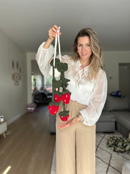Woman holding a crocheted strawberry plant decorative item in a living room.
