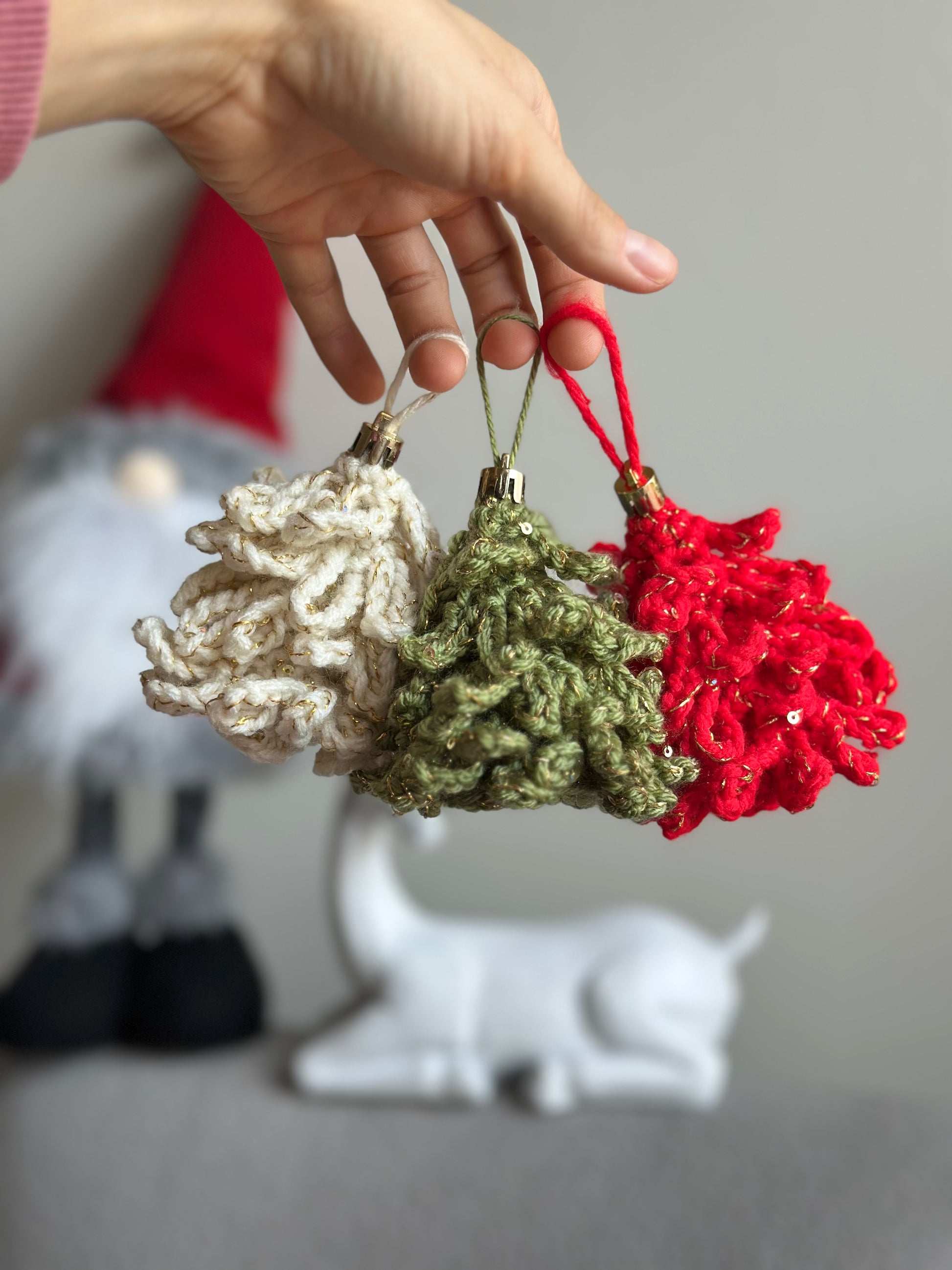Hand holding three crochet Christmas tree ornaments in festive colors red, green, and cream