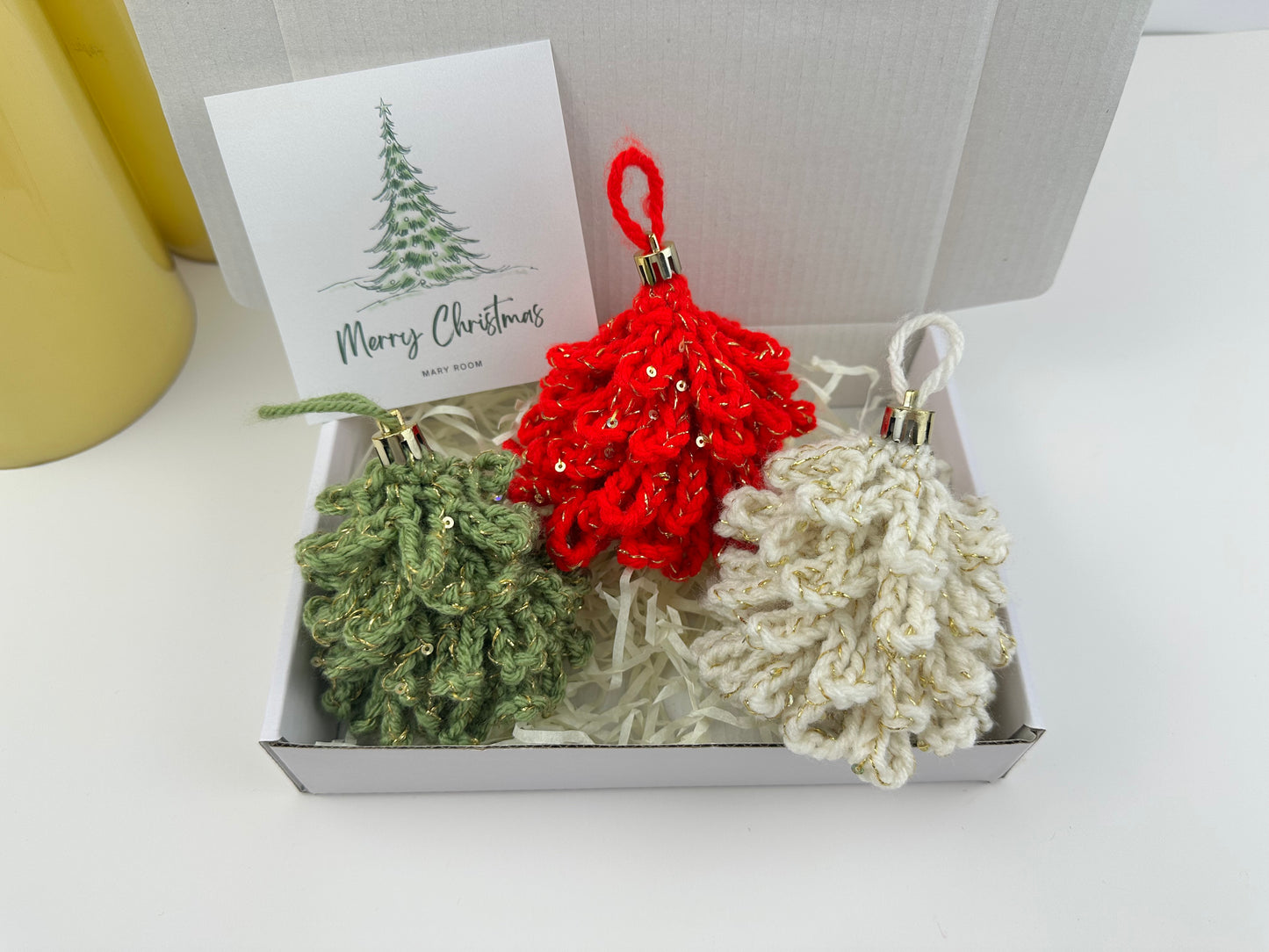 Set of three handmade crochet Christmas tree ornaments in red, green, and cream with Merry Christmas card in gift box