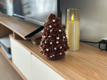 Handmade crochet brown Christmas tree with pearls on a wooden table next to a candle