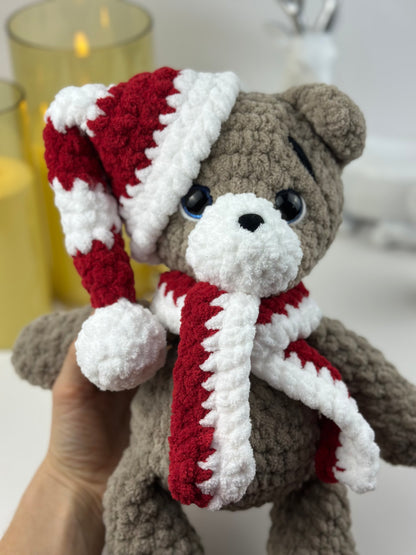 Crochet holiday teddy bear plush toy in red and white winter outfit, displayed on a cozy background.