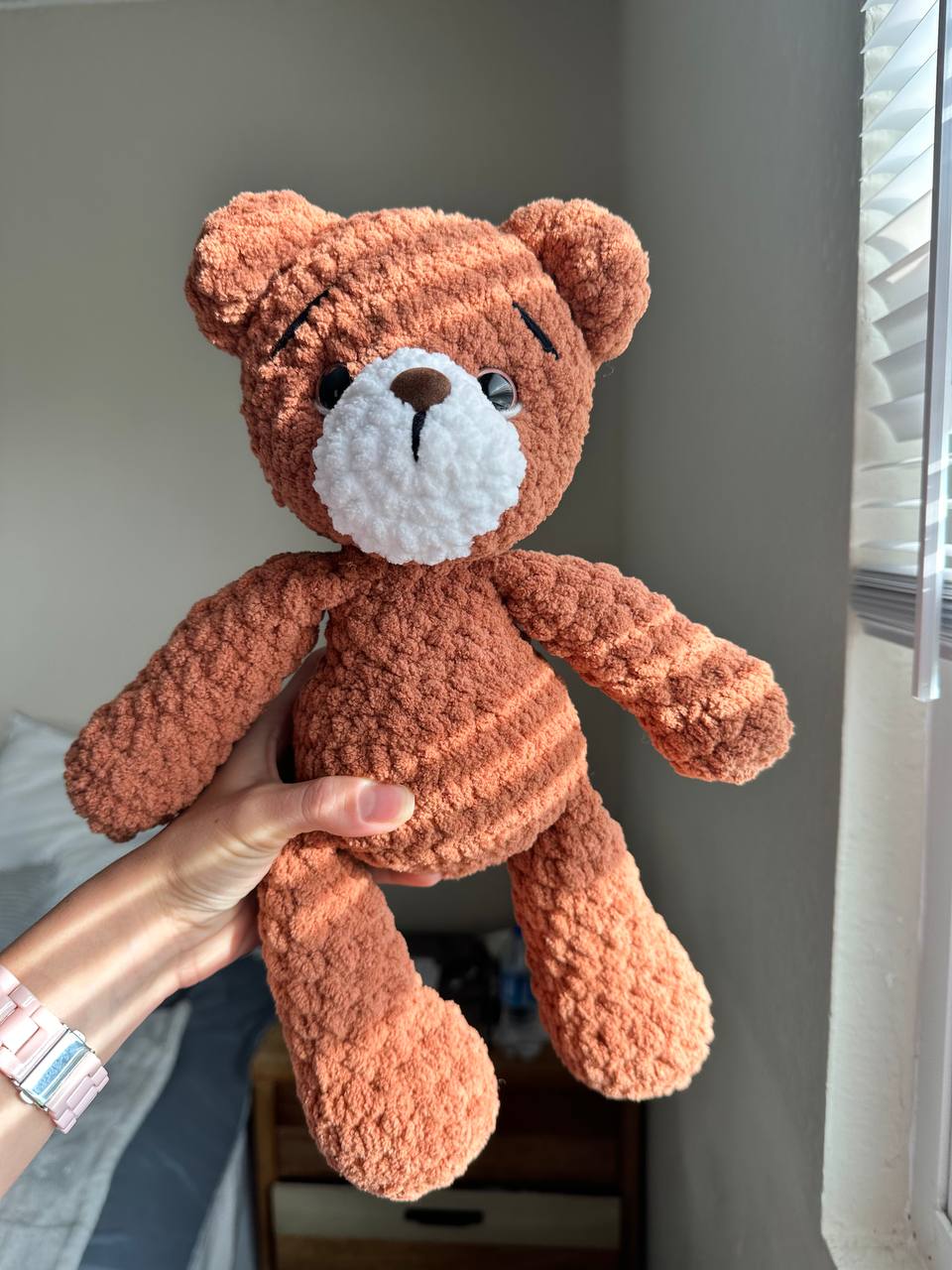 Handmade brown crochet teddy bear sitting on a chair in natural light.