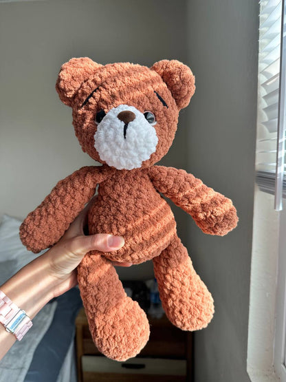 Handmade brown crochet teddy bear sitting on a chair in natural light.