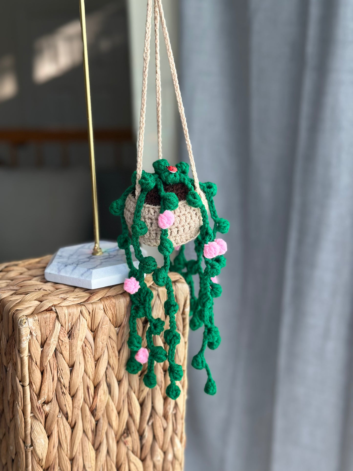 Crocheted string of pearls plant decoration hanging on a woven surface with a neutral background