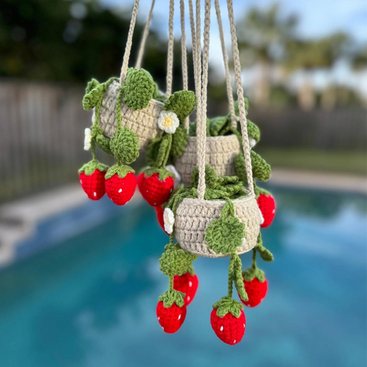 Crochet hanging strawberry plant with white flowers and green leaves in handmade pot