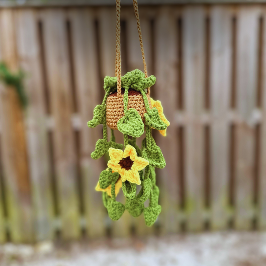 Crochet hanging sunflower plant with yellow flower petals and green vine in cream pot