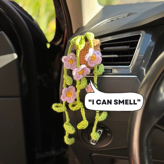 Car air freshener with floral design and 'I can smell' text inside a car.