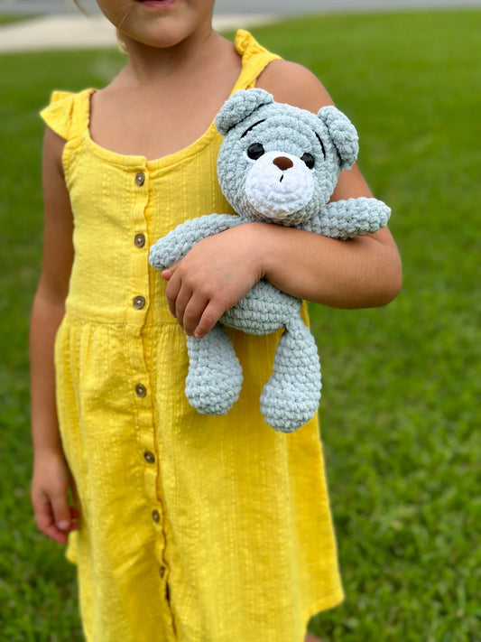 Handmade crochet teddy bear in light grey plush yarn held by a child in a yellow dress.