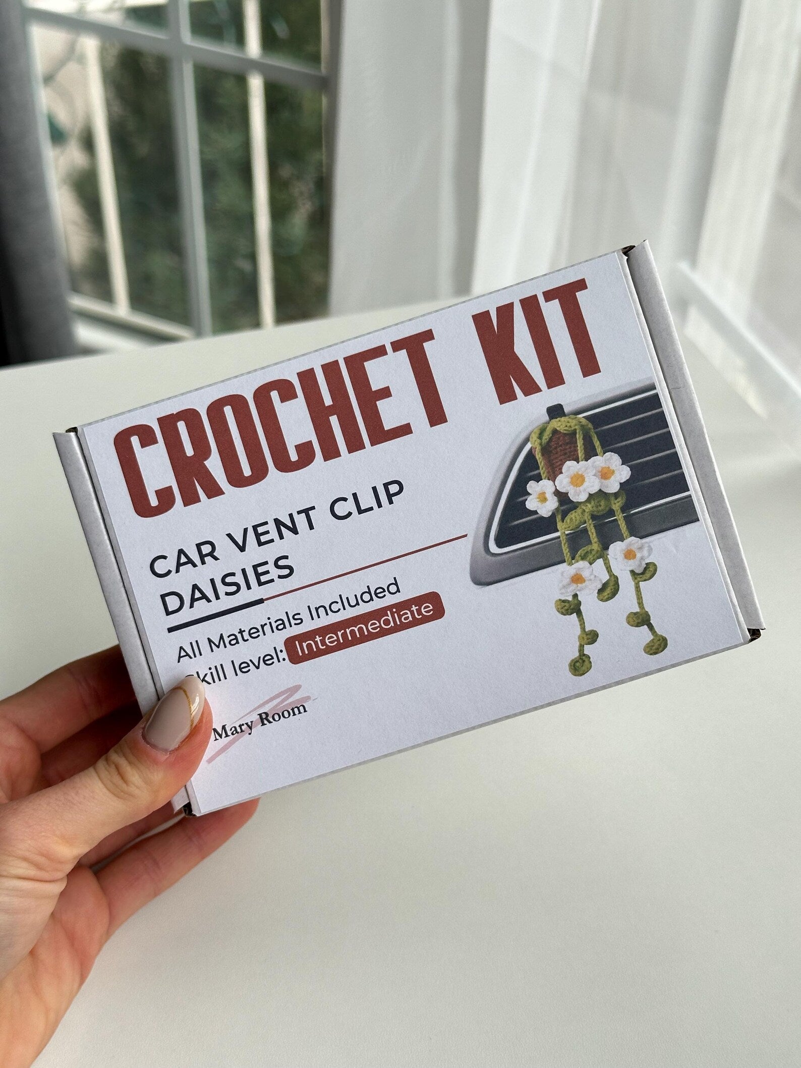 Complete crochet kit components displayed on white background: yarn, pattern card, sachet, hook, and accessories