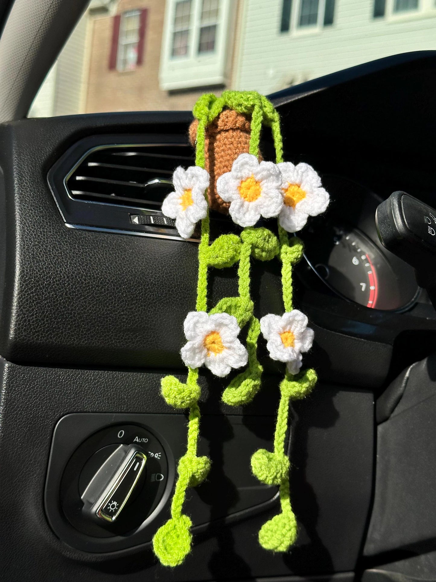 Crocheted daisy car vent clip hanging from dashboard in sunlight. crochet diy project, crochet kit