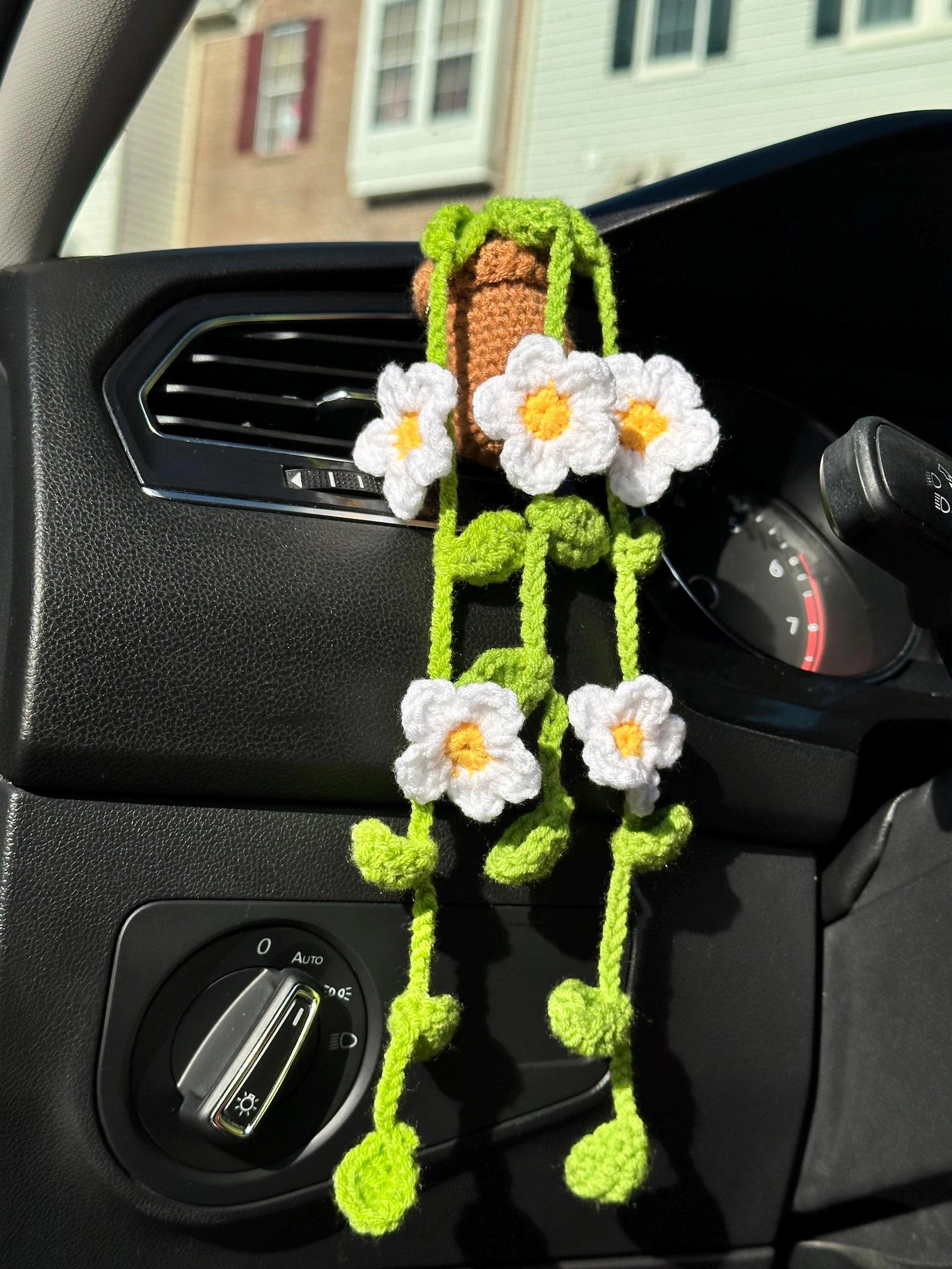 Crocheted daisy car vent clip hanging from dashboard in sunlight. crochet diy project, crochet kit