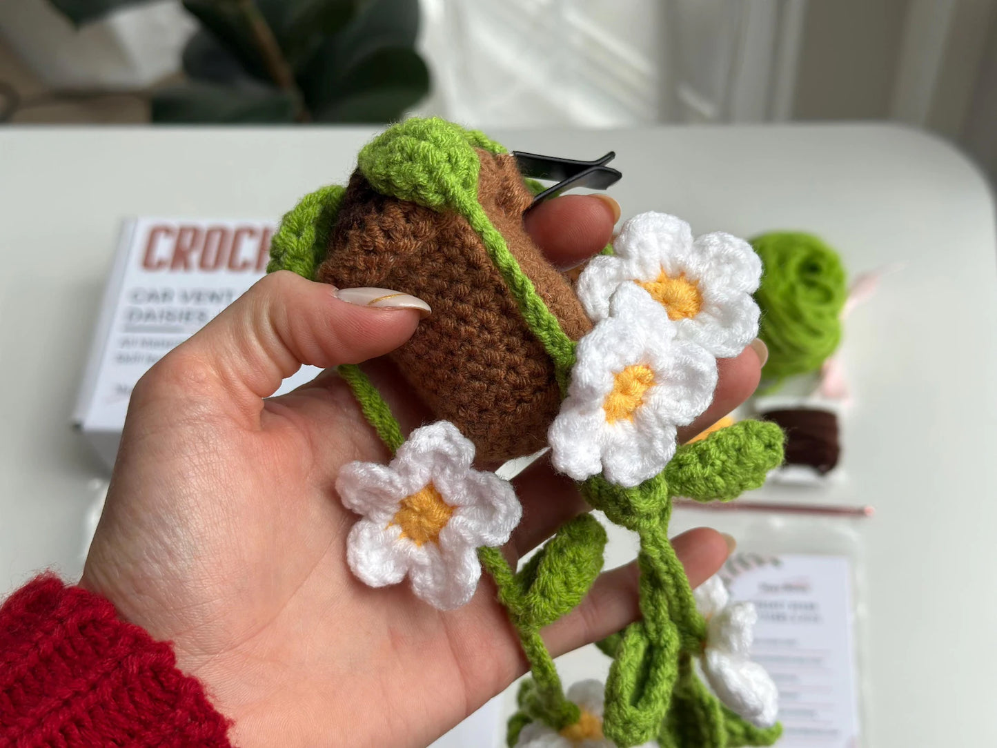 Close-up of hand holding the crocheted plant with daisies and clip