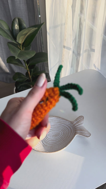Hand holding crocheted carrot acrylic clicker anti-stress near a window with play button icon for crochet tutorial video.